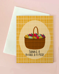 Greeting card with a basket of fruits and vegetables illustration and text 'Thanks a Bushel & A Peck' on a yellow plaid background.